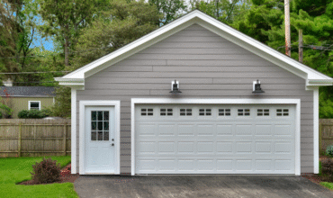 Detached garage with gray siding, two garage doors, and a side entrance, surrounded by green landscaping, emphasizing home improvement and custom construction services in Michigan.