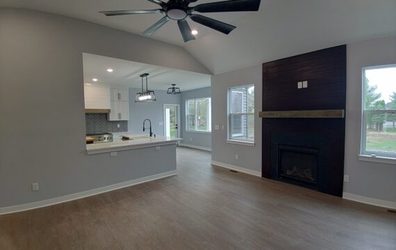 Modern living room with open kitchen layout, featuring a ceiling fan, fireplace, and large windows for natural light, illustrating potential home addition designs for Michigan homeowners.